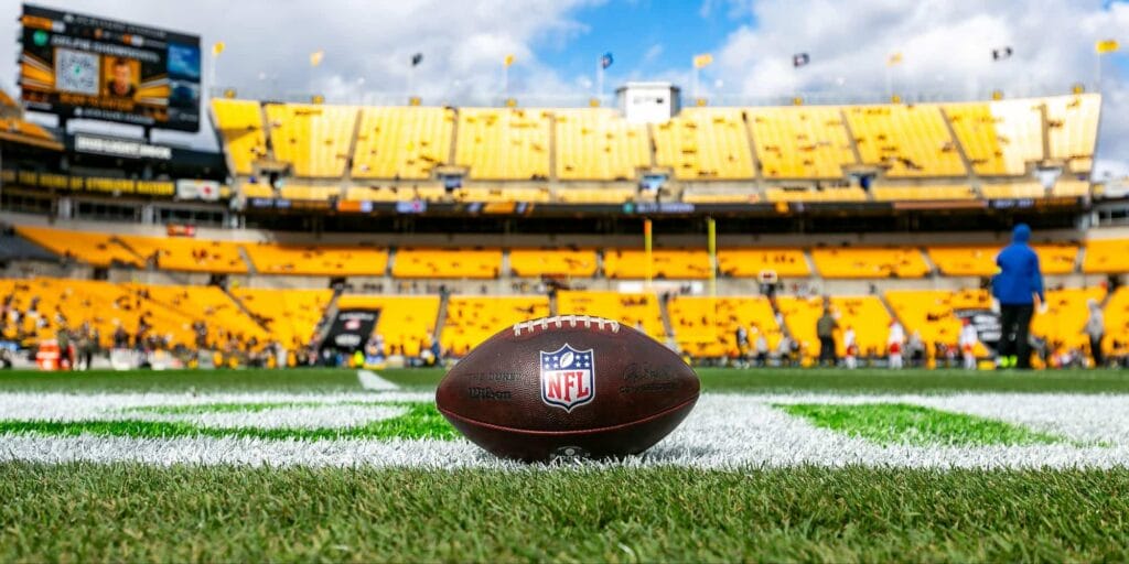 An NFL football in a stadium on a green field and yellow seats