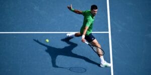 Novak Djokovic hitting a ball at the Australian Open wearing a green shirt and blue shorts