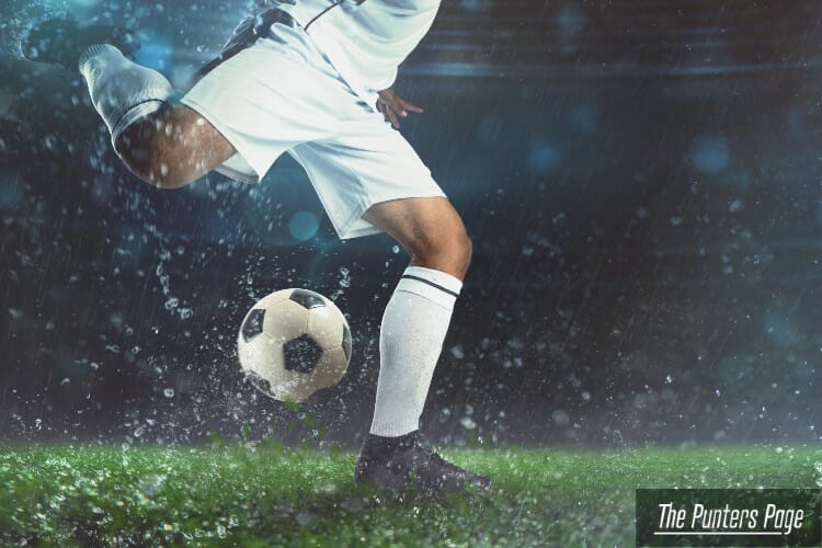 Image of a player about to shoot a football ball in a stadium during night time while raining